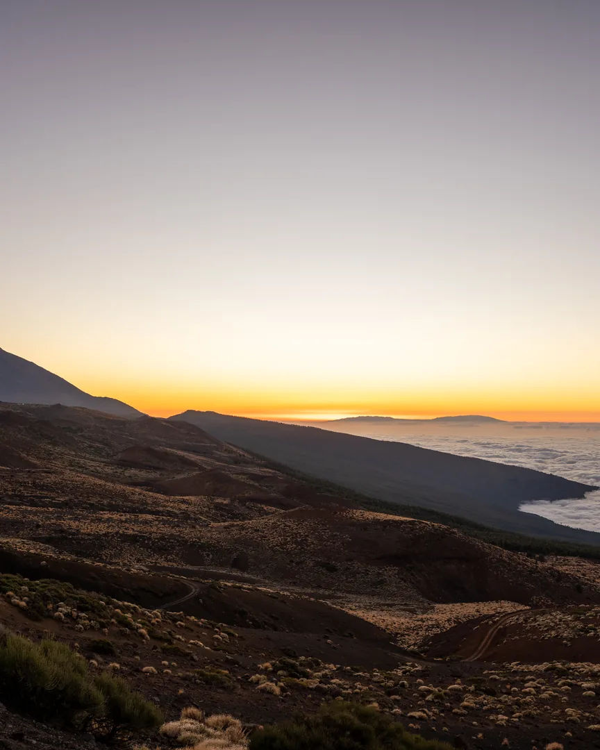 Tramonto dorato sopra un mare di nuvole, con il profilo di una montagna in lontananza