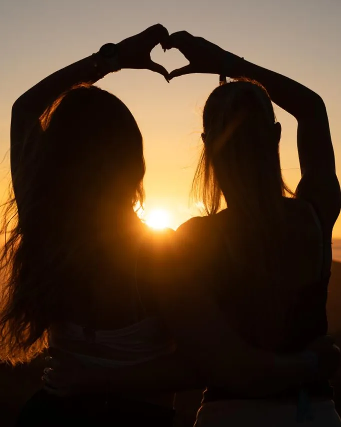 Sagoma di due persone che formano un cuore con le mani, in controluce al tramonto